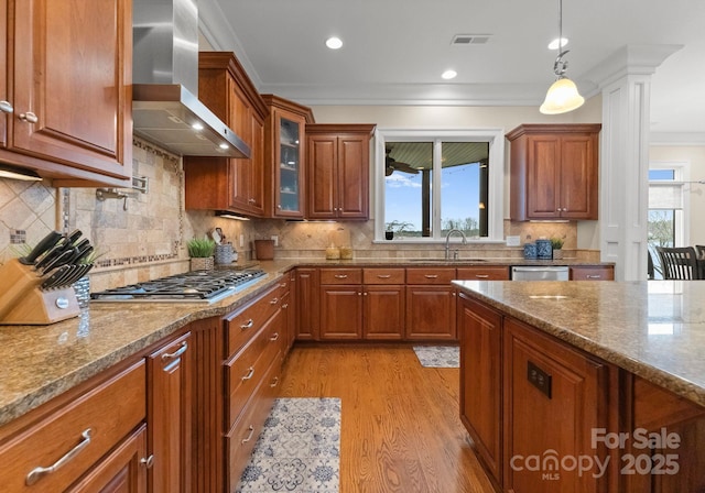 kitchen featuring light stone countertops, brown cabinetry, a sink, appliances with stainless steel finishes, and wall chimney range hood