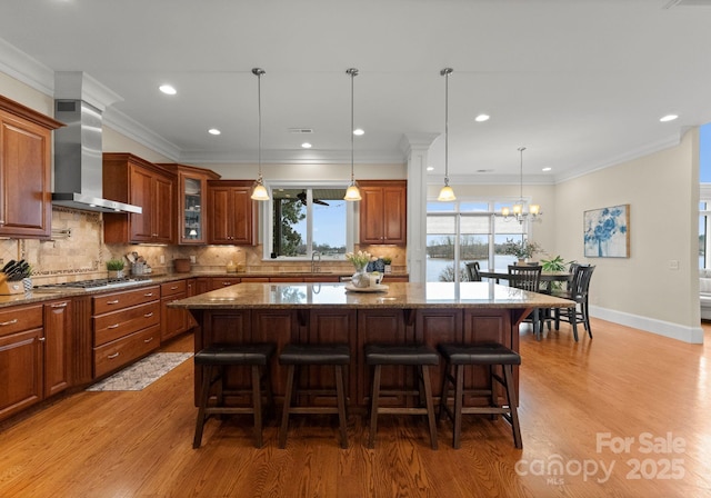 kitchen with a kitchen breakfast bar, a kitchen island, wall chimney range hood, and stainless steel gas stovetop