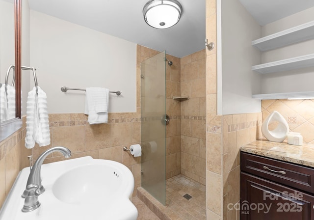 full bath featuring wainscoting, a shower stall, tile walls, and a sink