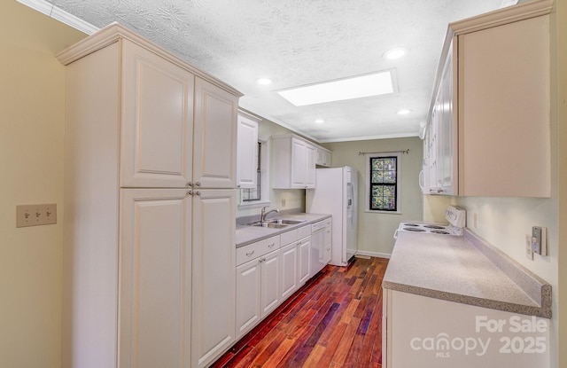 kitchen with a sink, a textured ceiling, dark wood-style floors, white appliances, and crown molding