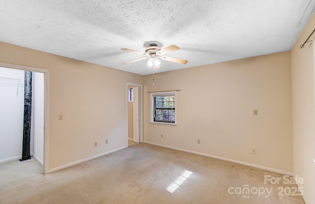 unfurnished bedroom featuring light carpet, a textured ceiling, a closet, baseboards, and a spacious closet