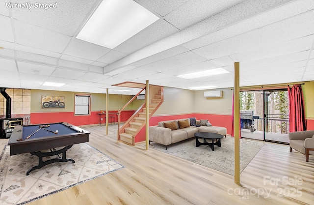 rec room featuring a paneled ceiling, wood finished floors, a wood stove, and a wall mounted AC