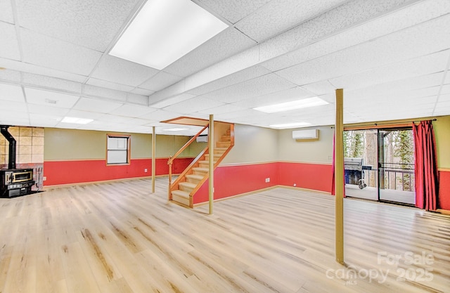 basement with stairway, a wall unit AC, a wood stove, and wood finished floors