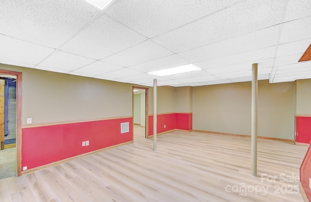 finished basement featuring wood finished floors, visible vents, a drop ceiling, and baseboards