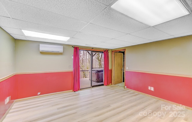 empty room with a wall mounted air conditioner, a paneled ceiling, baseboards, and wood finished floors