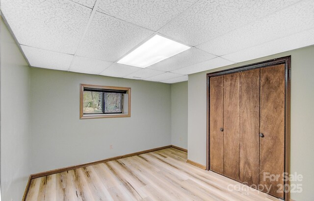 unfurnished bedroom featuring a closet, baseboards, a paneled ceiling, and light wood-style floors