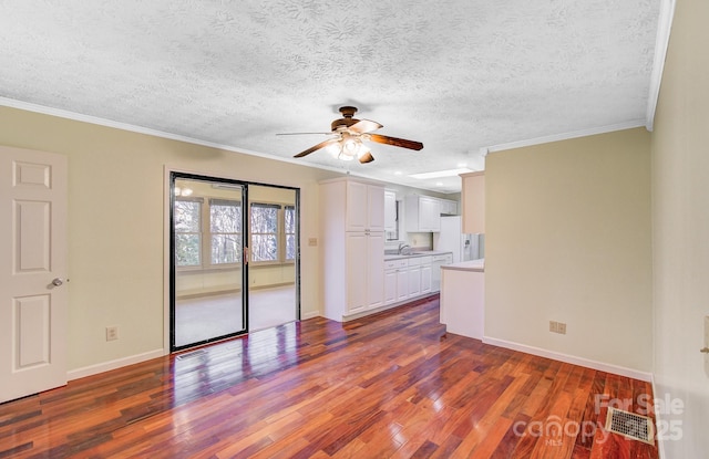 unfurnished living room featuring dark wood finished floors, a sink, baseboards, and ornamental molding