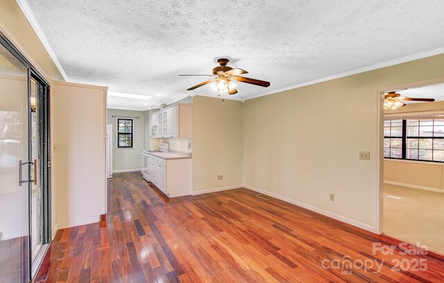 unfurnished living room with a wealth of natural light, visible vents, wood-type flooring, and crown molding