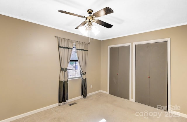 unfurnished bedroom with ornamental molding, baseboards, visible vents, and multiple closets