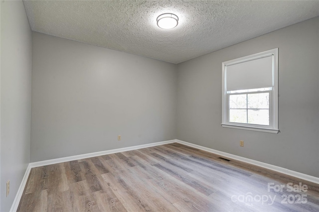 unfurnished room with visible vents, baseboards, a textured ceiling, and wood finished floors