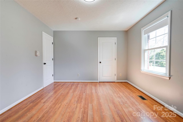 unfurnished room with baseboards, visible vents, light wood finished floors, and a textured ceiling