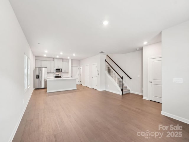 unfurnished living room with recessed lighting, stairway, baseboards, and light wood finished floors