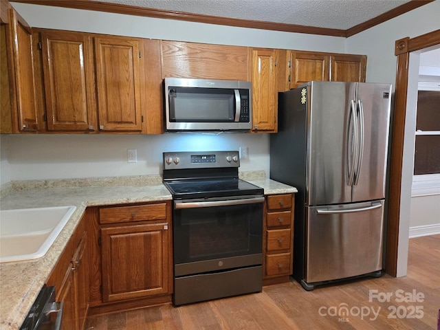 kitchen featuring crown molding, light wood-style floors, brown cabinets, and stainless steel appliances