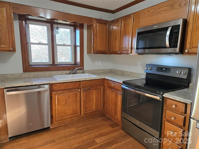 kitchen featuring light countertops, light wood-type flooring, appliances with stainless steel finishes, brown cabinetry, and a sink