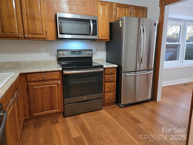 kitchen featuring visible vents, light wood finished floors, appliances with stainless steel finishes, brown cabinetry, and light countertops