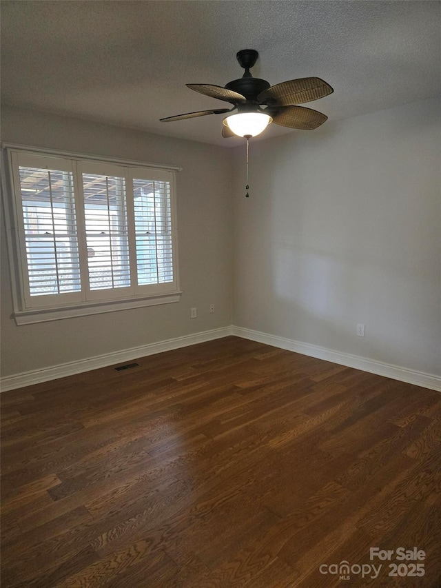 spare room with visible vents, baseboards, dark wood-type flooring, and ceiling fan