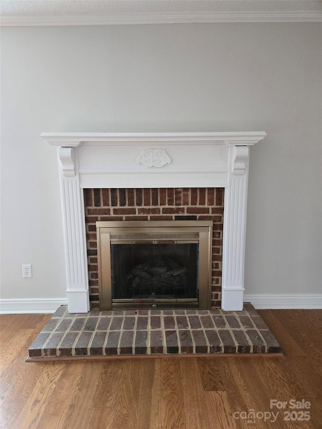 room details with a brick fireplace, wood finished floors, baseboards, and ornamental molding