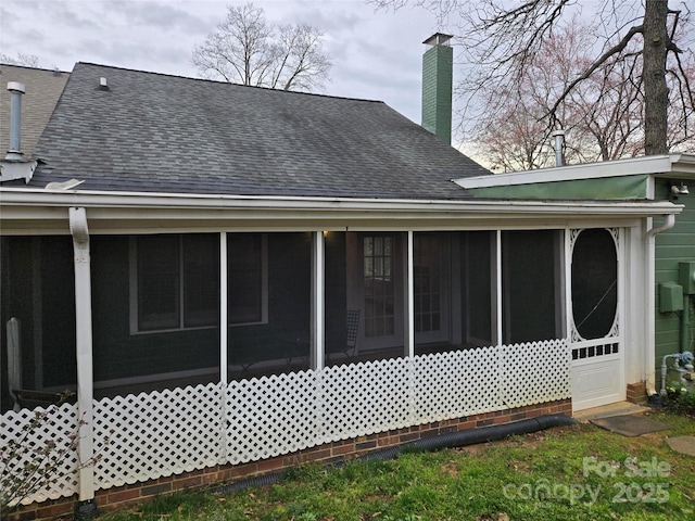 back of house with a sunroom, roof with shingles, and a chimney