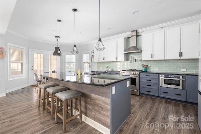 kitchen featuring dark countertops, stainless steel appliances, wall chimney range hood, and a sink