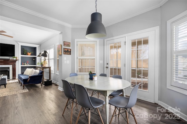 dining space featuring dark wood-style floors, a fireplace, crown molding, baseboards, and ceiling fan