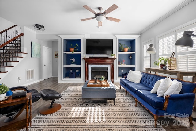 living room with visible vents, wood finished floors, stairs, and ornamental molding