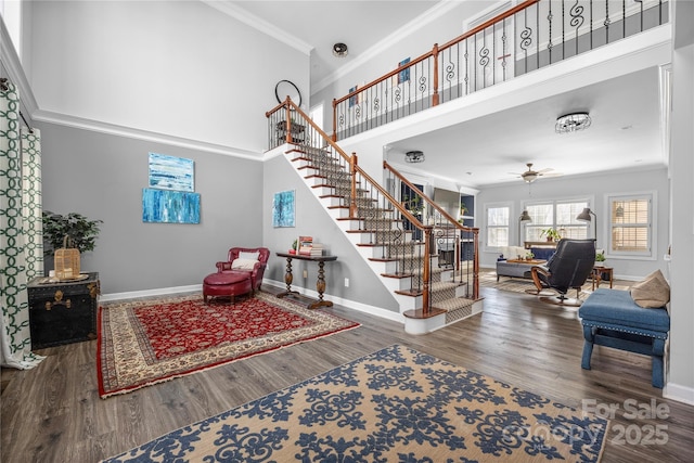 living area with stairs, a high ceiling, wood finished floors, and crown molding