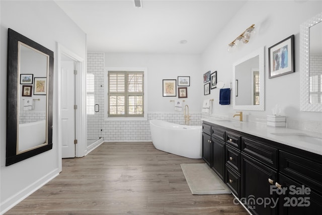 bathroom featuring a freestanding tub, a sink, wood finished floors, tile walls, and double vanity