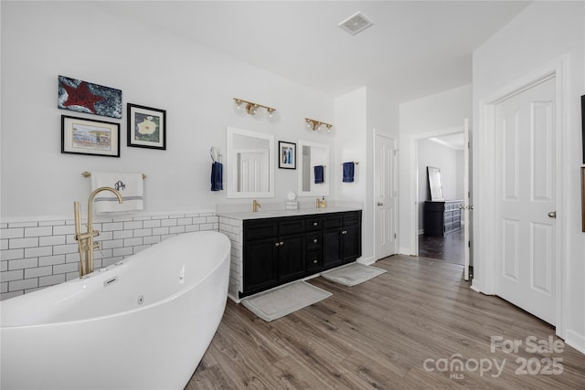 full bathroom with wood finished floors, visible vents, double vanity, a sink, and a freestanding bath