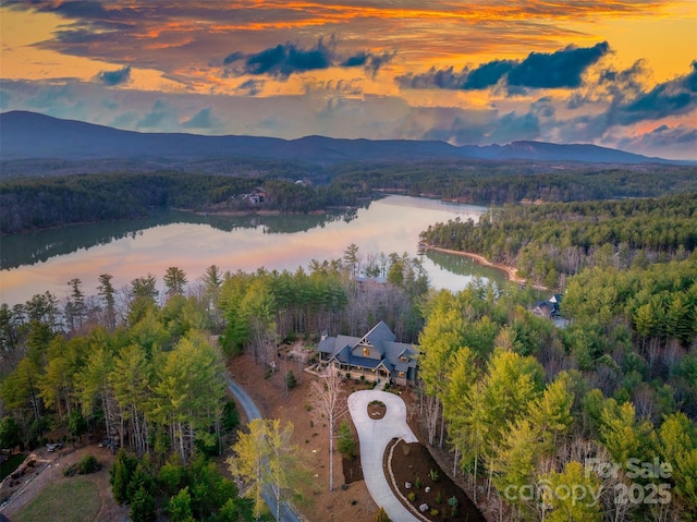 aerial view at dusk with a water and mountain view and a wooded view