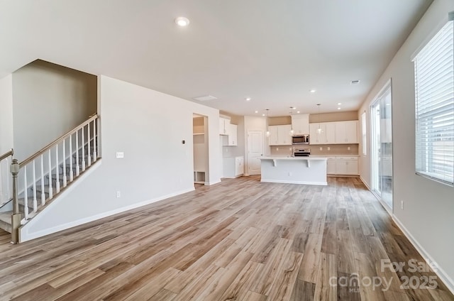 unfurnished living room with stairs, recessed lighting, baseboards, and light wood finished floors