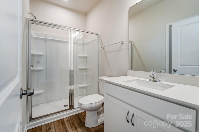 bathroom featuring wood finished floors, toilet, a stall shower, and vanity