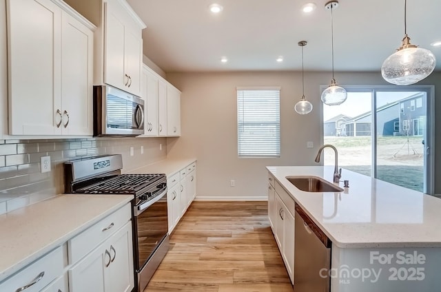 kitchen featuring a center island with sink, a sink, stainless steel appliances, light wood-style floors, and backsplash