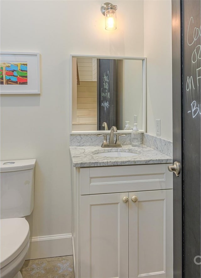 half bath featuring vanity, toilet, and baseboards