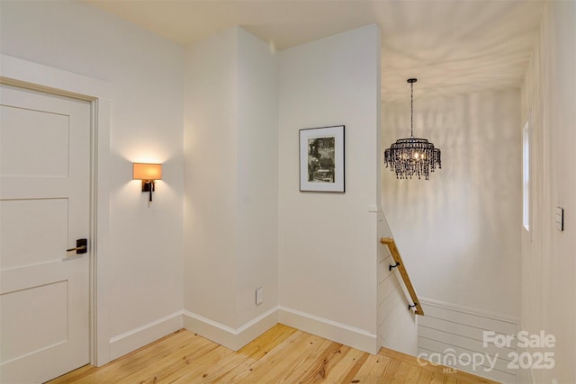 hall featuring baseboards, an upstairs landing, a notable chandelier, and light wood finished floors