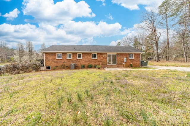 rear view of property with a yard, brick siding, and central AC