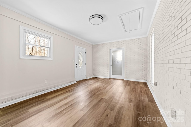 interior space with brick wall, crown molding, baseboards, and wood finished floors