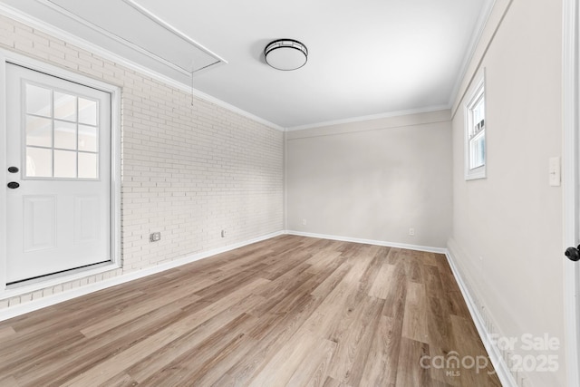 empty room with brick wall, attic access, crown molding, and wood finished floors