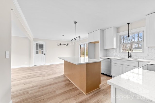 kitchen with a sink, light wood-style floors, stainless steel dishwasher, tasteful backsplash, and a chandelier