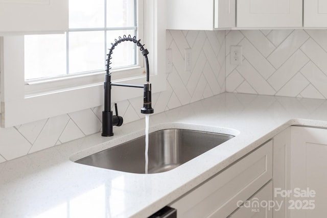 room details with a sink, light stone countertops, backsplash, and white cabinets