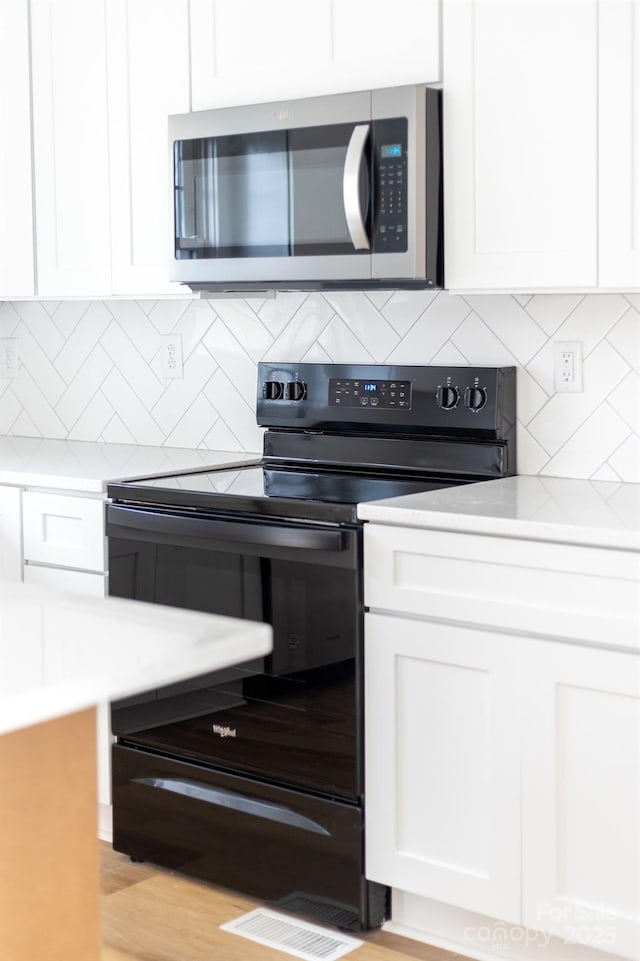 kitchen featuring electric range, white cabinetry, light countertops, and stainless steel microwave