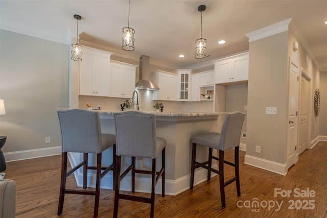 kitchen featuring crown molding, glass insert cabinets, wall chimney range hood, dark wood-style floors, and white cabinets