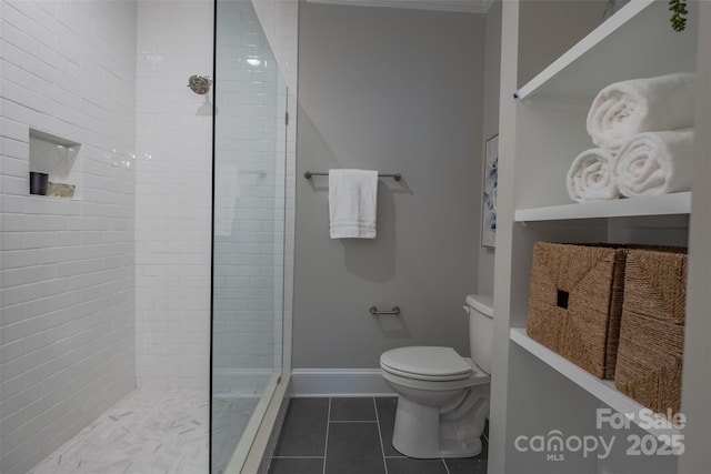 bathroom with tile patterned flooring, toilet, baseboards, and tiled shower