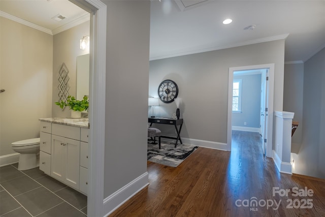 hall with dark wood-style floors, visible vents, baseboards, and ornamental molding