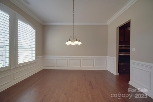 unfurnished dining area featuring dark wood-style floors, a notable chandelier, a wainscoted wall, and ornamental molding