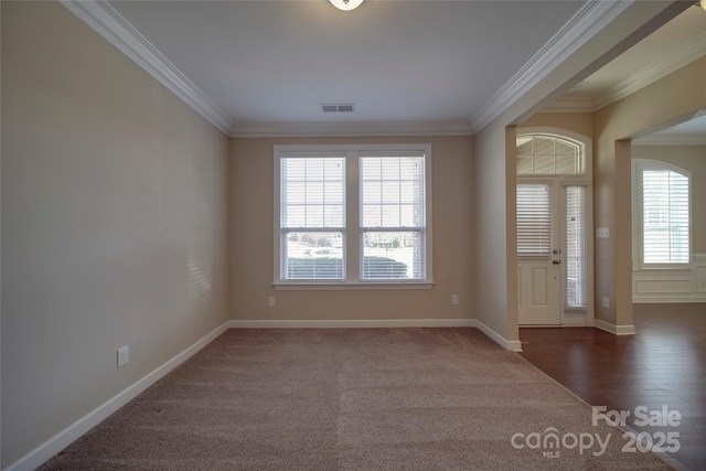 carpeted foyer with wood finished floors, baseboards, visible vents, and ornamental molding