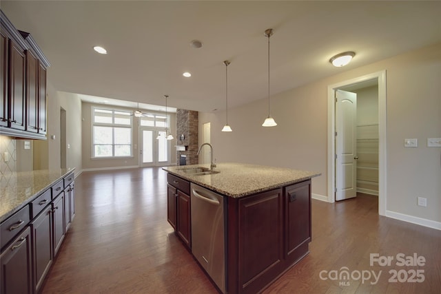 kitchen with dishwasher, light stone counters, a stone fireplace, dark wood-style floors, and a sink