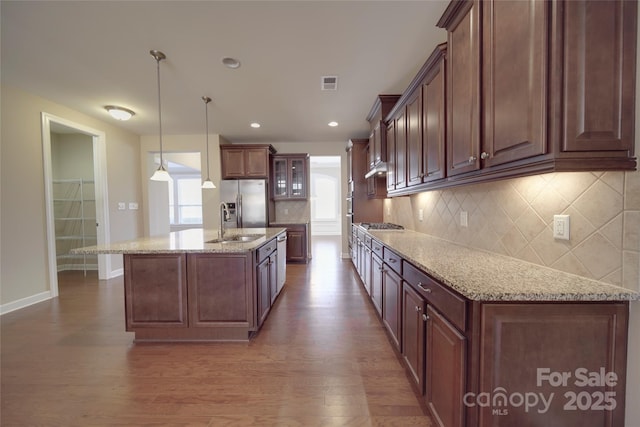 kitchen with visible vents, a kitchen island with sink, dark wood-style floors, stainless steel appliances, and light stone countertops