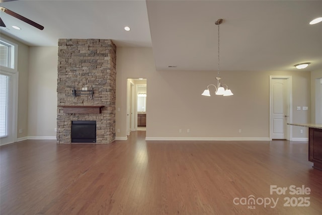 unfurnished living room with ceiling fan with notable chandelier, a fireplace, baseboards, and wood finished floors