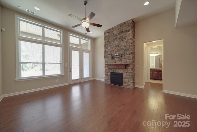 unfurnished living room featuring visible vents, ceiling fan, baseboards, a stone fireplace, and dark wood-style flooring