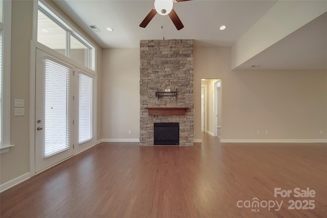 unfurnished living room featuring wood finished floors, recessed lighting, a stone fireplace, baseboards, and ceiling fan